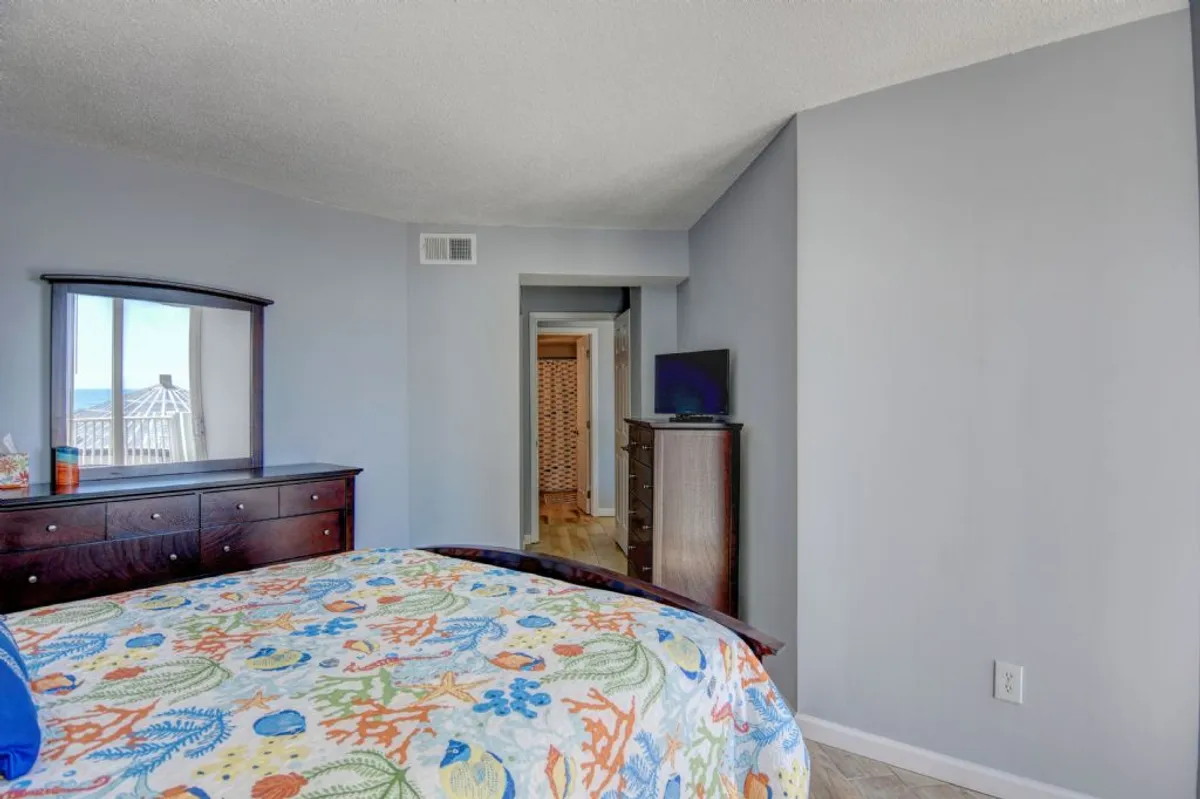 A cozy bedroom with colorful bedding, a wooden dresser, and a mirror reflecting gentle light. The space feels inviting and personal, perfect for guests seeking comfort and privacy. A television is set up for entertainment.