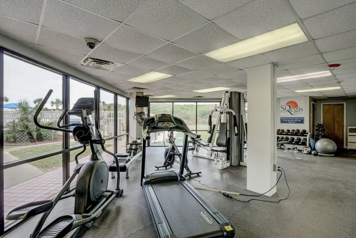 A bright, well-equipped fitness center with treadmills, an elliptical, strength training equipment, and large windows that let in natural light. The energetic setting encourages active routines and wellness.