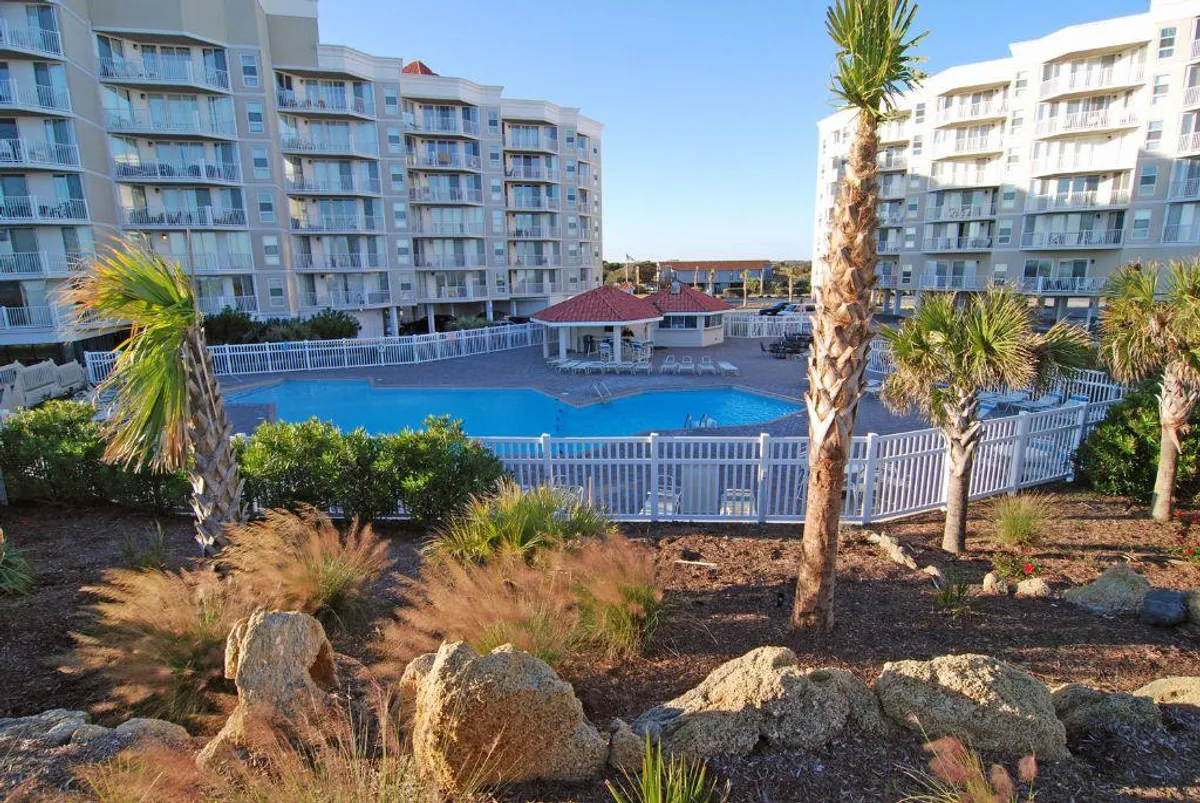 A vibrant pool area featuring a sparkling swimming pool surrounded by palm trees, a poolside gazebo, and the facade of the resort building. The scene is lively yet relaxed, inviting guests to swim, sunbathe, or gather for social events.