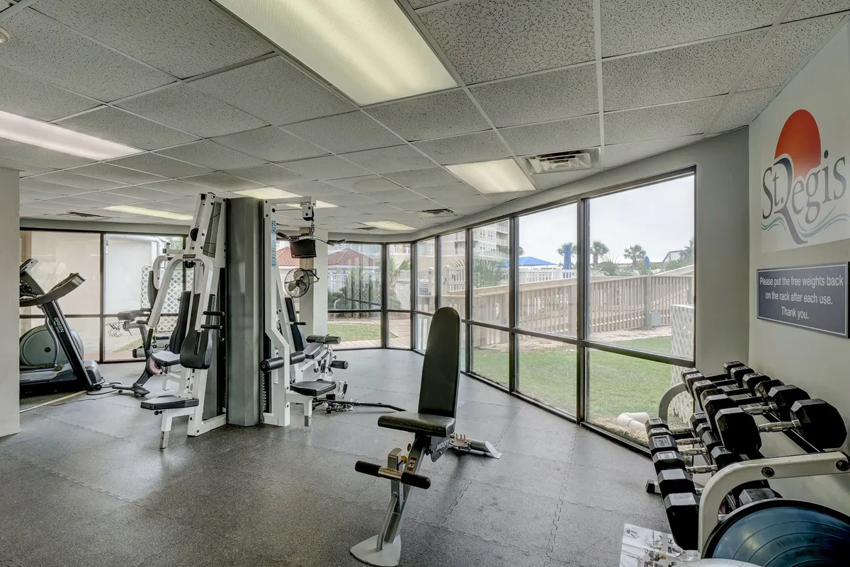 Inside the resort's fitness center, a row of modern exercise machines and a dumbbell rack face large windows overlooking the grounds. The setting is bright and inviting, designed for solo or shared workouts and wellness routines.