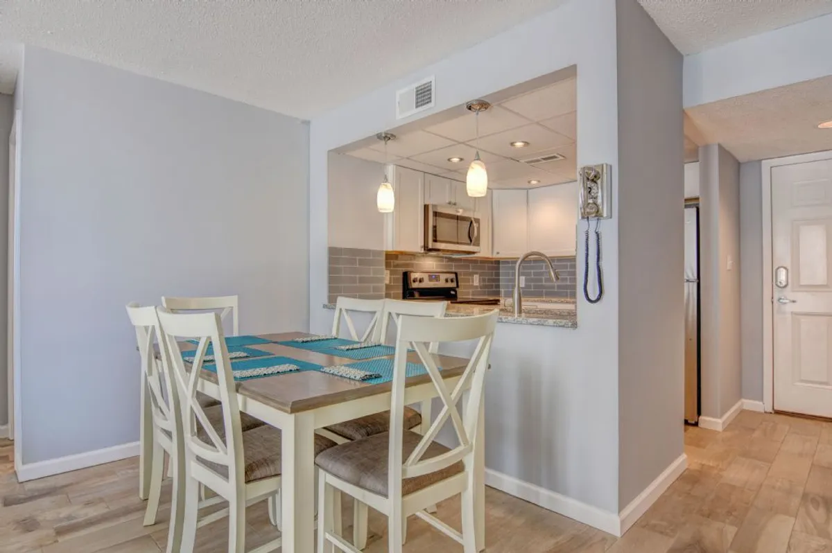An adjacent dining area featuring a beautiful dining table set under warm pendant lighting, with the kitchen and its countertops visible in the background. The mood is cozy and welcoming, ideal for both family feasts and special celebrations.