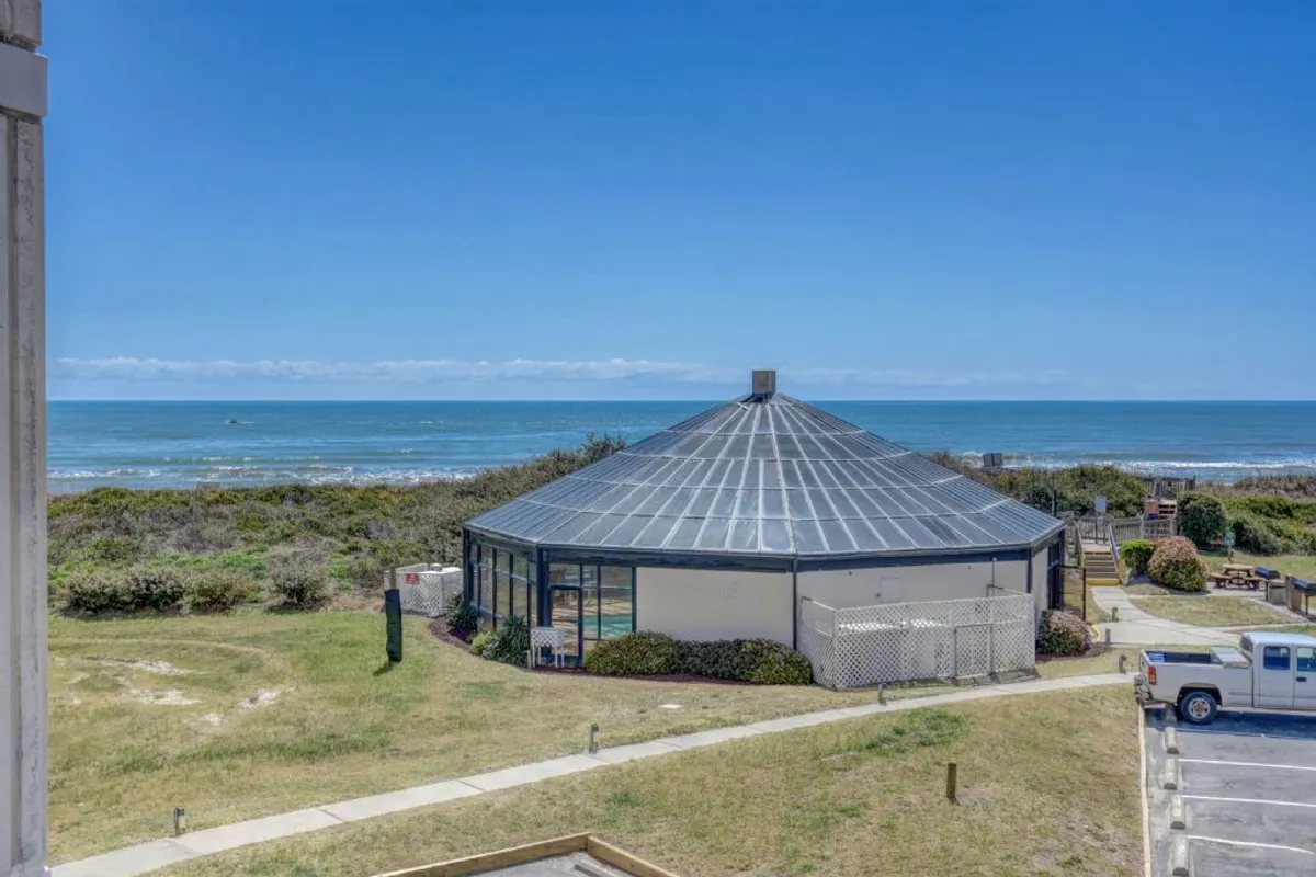 An inviting exterior shot of the resort's circular building set against a stunning ocean view. The landscaped area in the foreground hints at relaxing walks, outdoor gatherings, and tranquil moments by the sea.