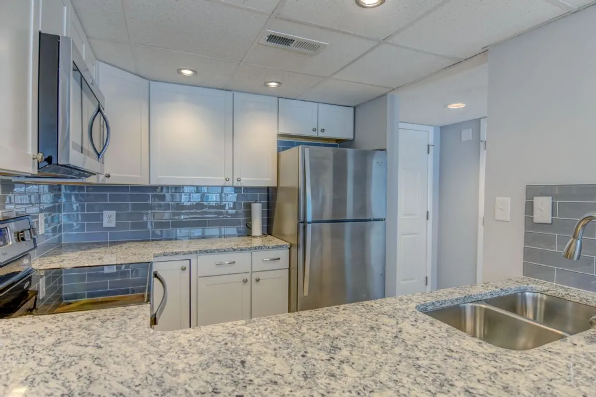 A stylish kitchen featuring sleek granite countertops, stainless steel appliances including a refrigerator and oven, and modern cabinetry. The countertop is uncluttered, showcasing its spaciousness and inviting functionality. Warm lighting enhances the inviting and functional atmosphere.
